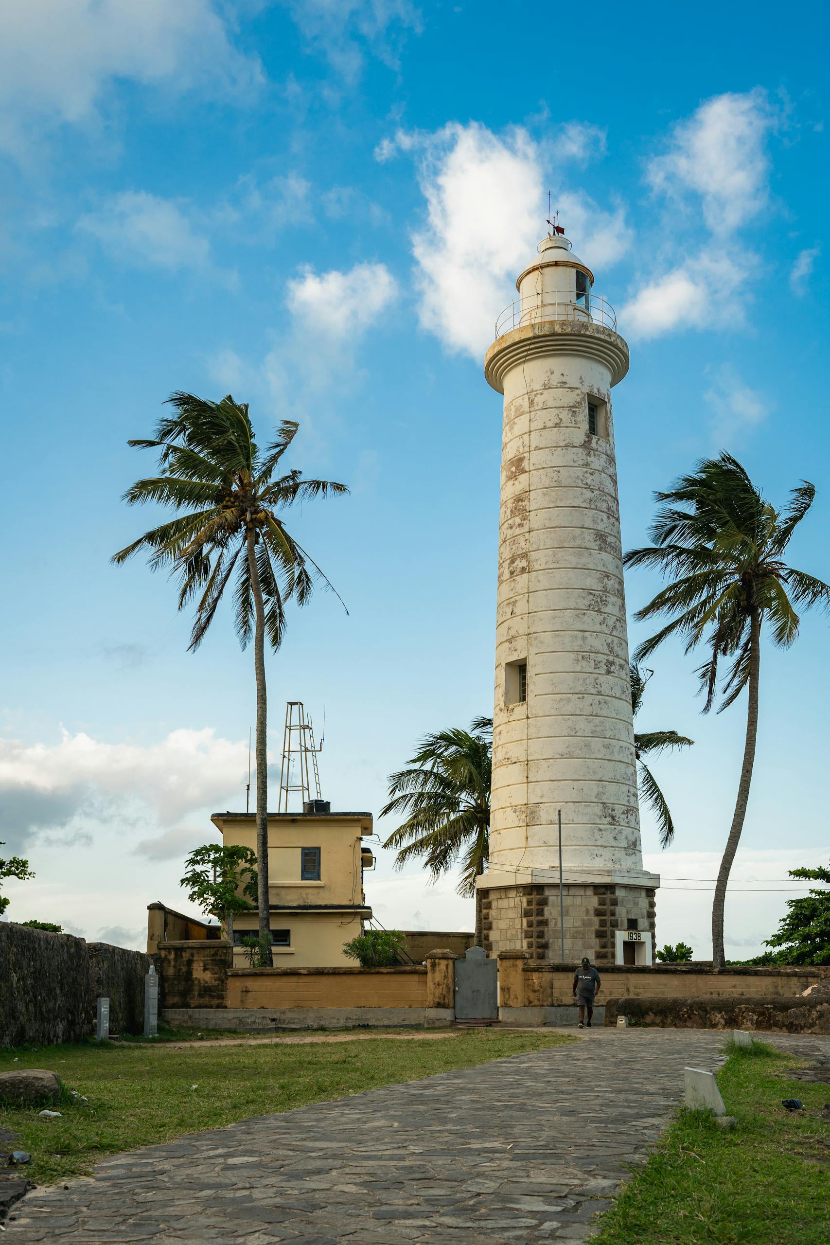 Scenic view of the Galle Lighthouse under a clear blue sky, surrounded by palm trees.